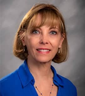 Headshot of Heidi Thibert. She is a middle aged white woman with short blonde hair. She is wearing a blue collared shirt and a beaded necklace